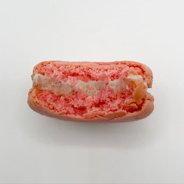 A strawberry macaron, bitten to show its filling